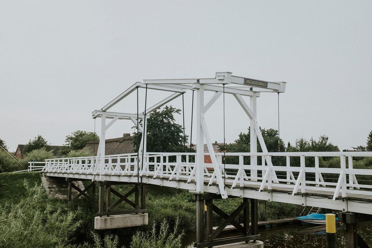 Weiße hölzerne Klappbrücke über einen Graben.