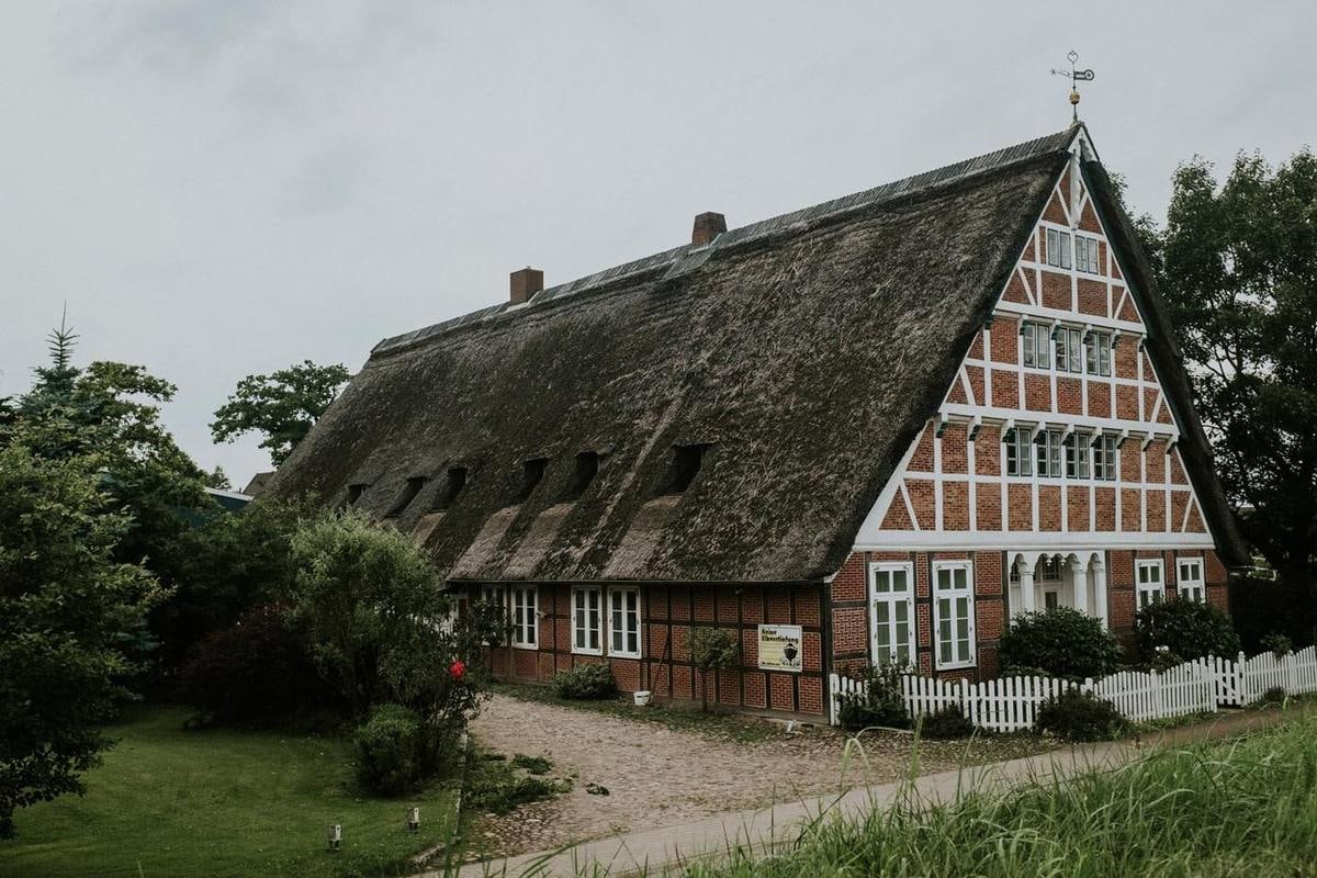 Langer Hof mit Reetdach hinter einem Gartenzaun.