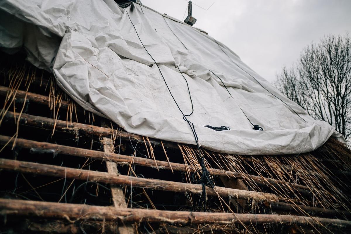 Freigelegte runde Holzlatten unter einer weißen Plane.