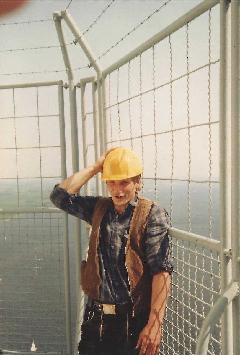 Ein Mann mit Schutzhelm steht in einem Gerüstkorb hoch über dem Boden.