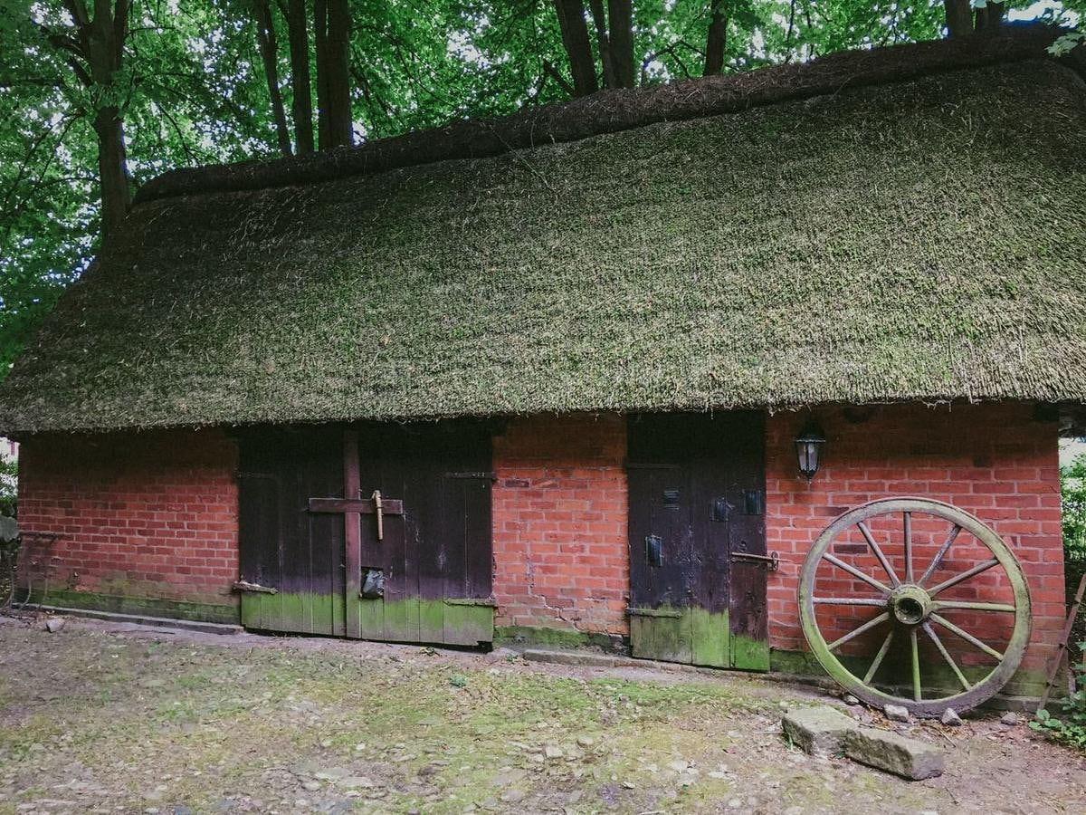Backsteinscheune mit Reetdach, davor ein Wagenrad.