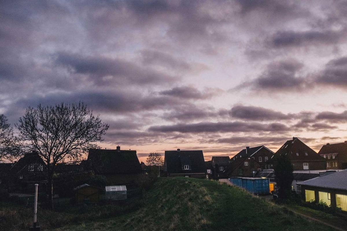 Häuser mit Reetdach hinter dem Deich unter Abendwolken.