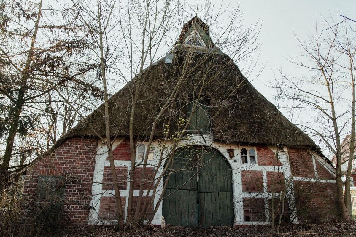 Fachwerkgiebel mit Torbogen unter einem moosigen Reetdach, kahle Bäume.