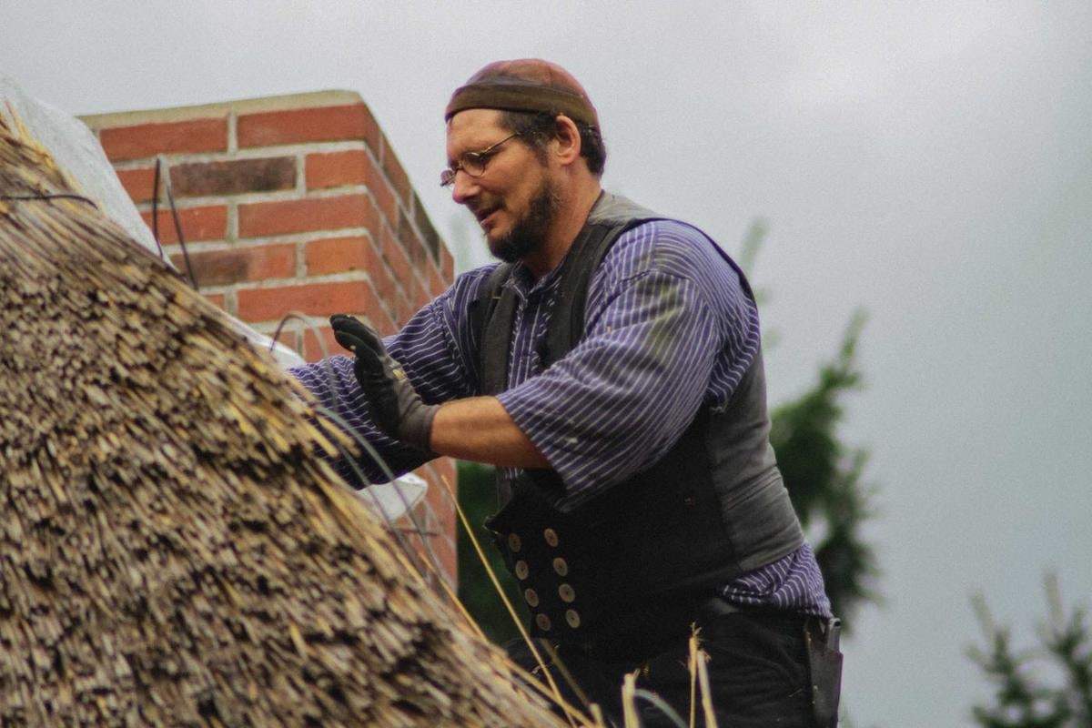 Handwerker arbeitet neben einem Backsteinschornstein am Reet.