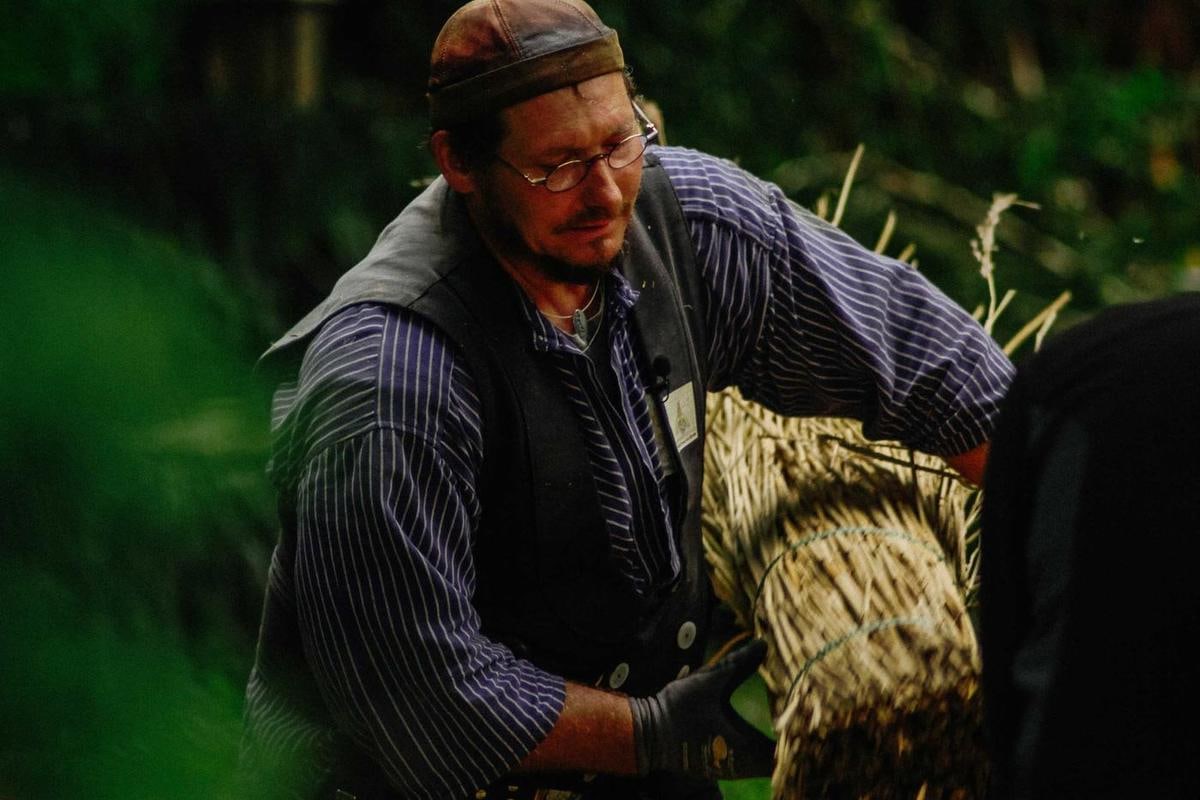 Handwerker in Weste mit einem Reetbund unter dem Arm.