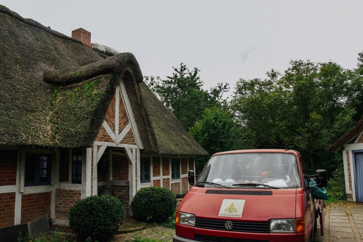 Fachwerkhaus mit Reetdach, davor ein roter Kleintransporter.
