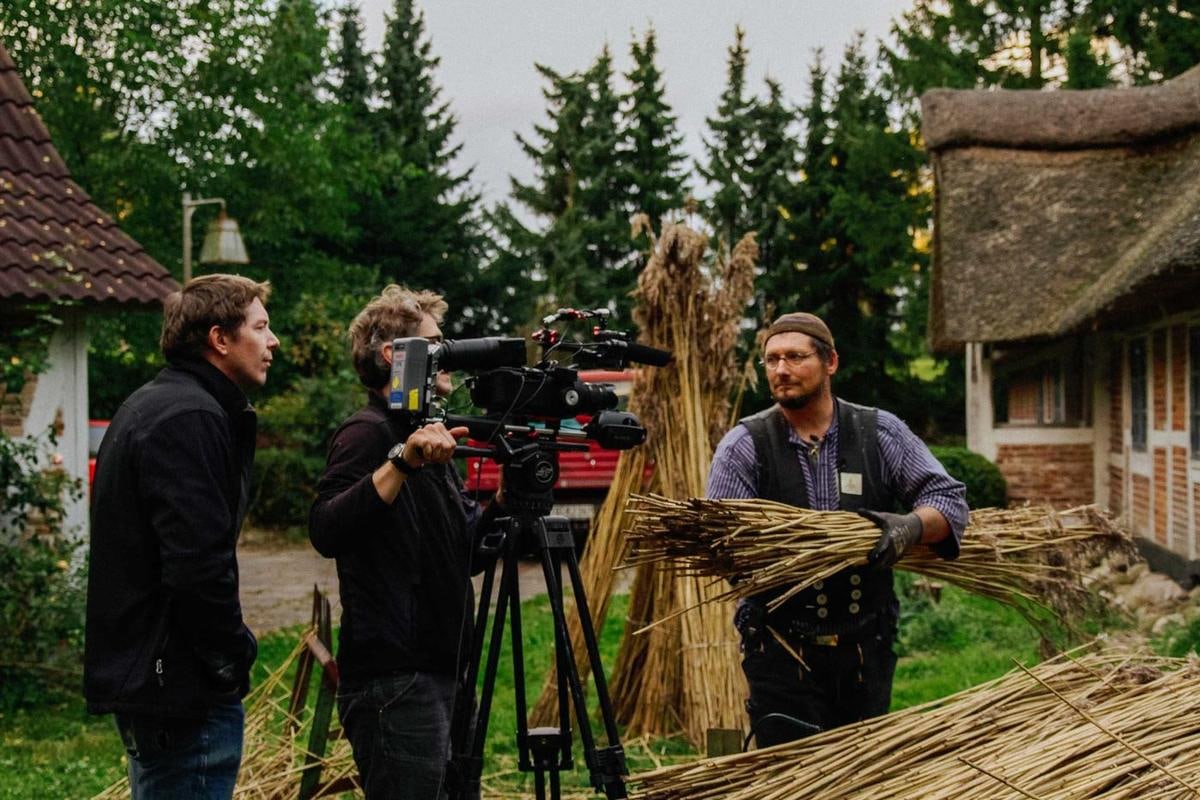 Ein Handwerker mit Reetbund wird im Garten gefilmt.