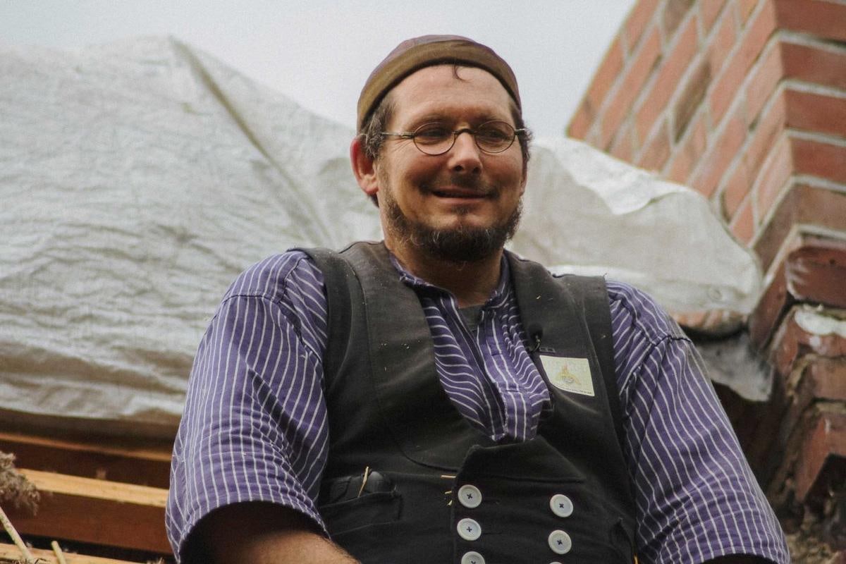 Lachender Mann mit Brille in Zunftweste vor einer Plane.