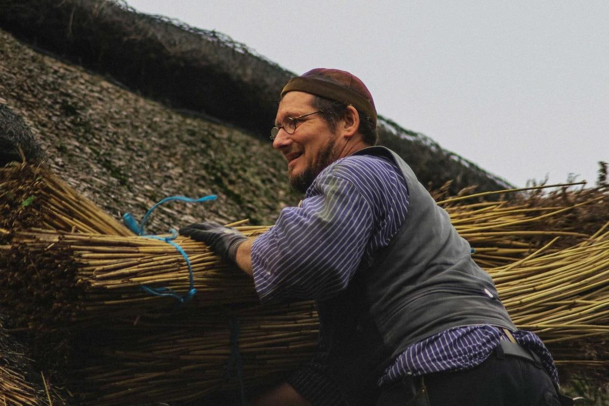 Handwerker greift lachend in ein Bund am Dach.