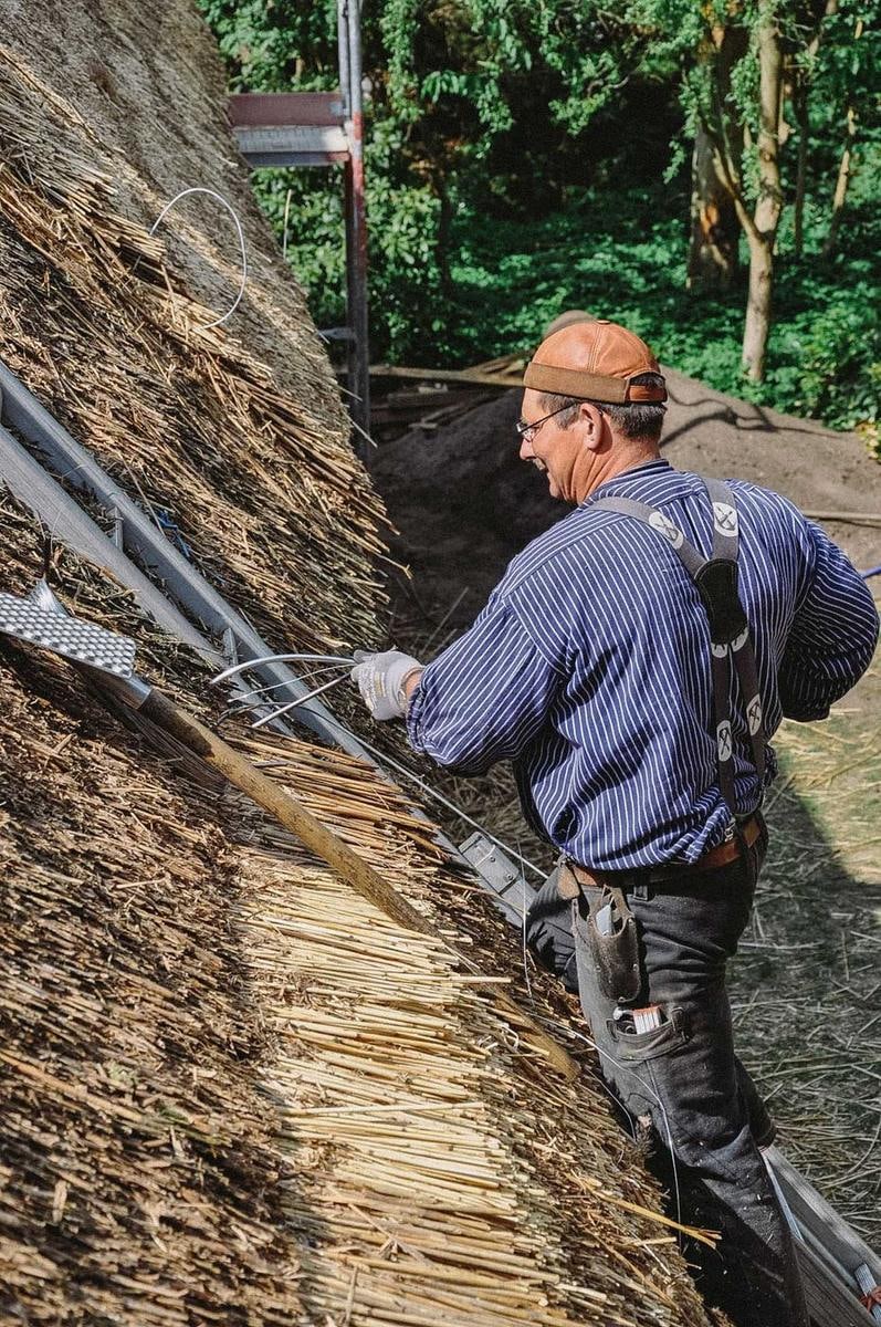 Ein Handwerker arbeitet an der Traufkante eines Reetdachs.