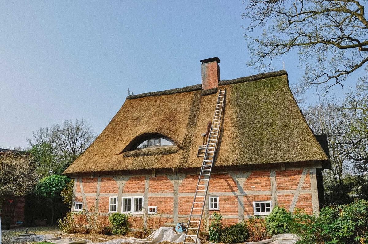 Haus mit Reetdach und Fledermausgaube, eine Leiter lehnt am Dach.