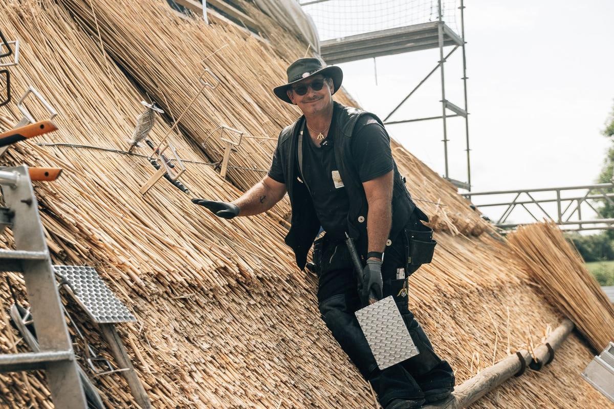 Handwerker steht auf dem Reet, das Klopfbrett in der Hand.