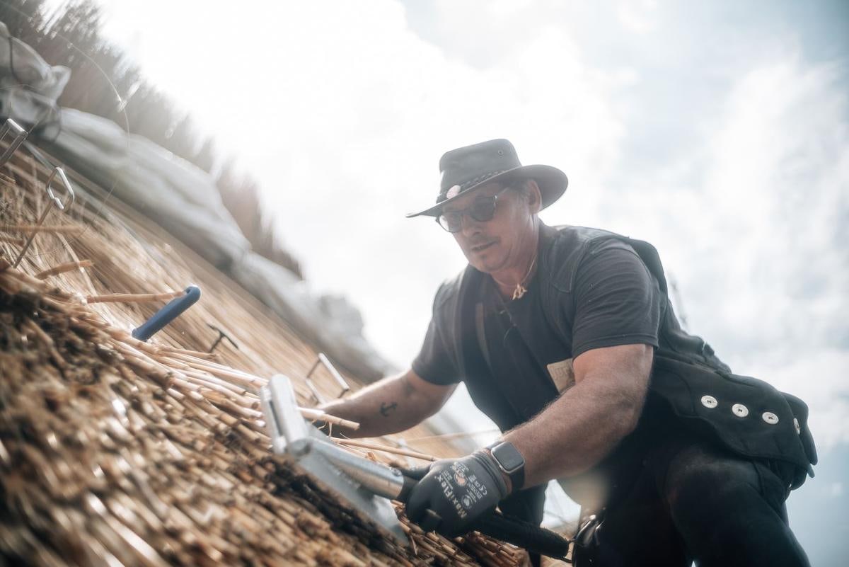 Handwerker richtet mit dem Werkzeug Halme aus.