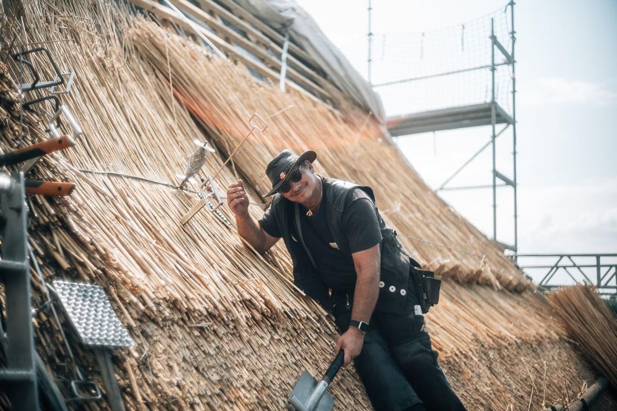 Handwerker mit Werkzeug auf einer großen Reetfläche.