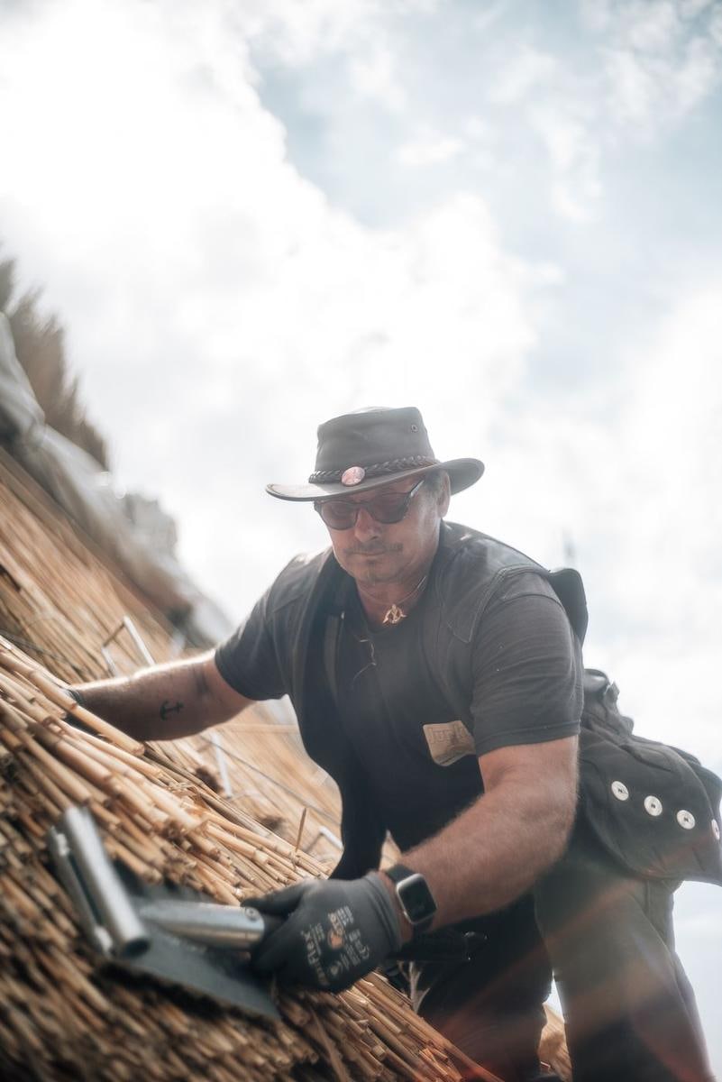 Handwerker mit Hut auf dem Reet vor weißem Himmel.