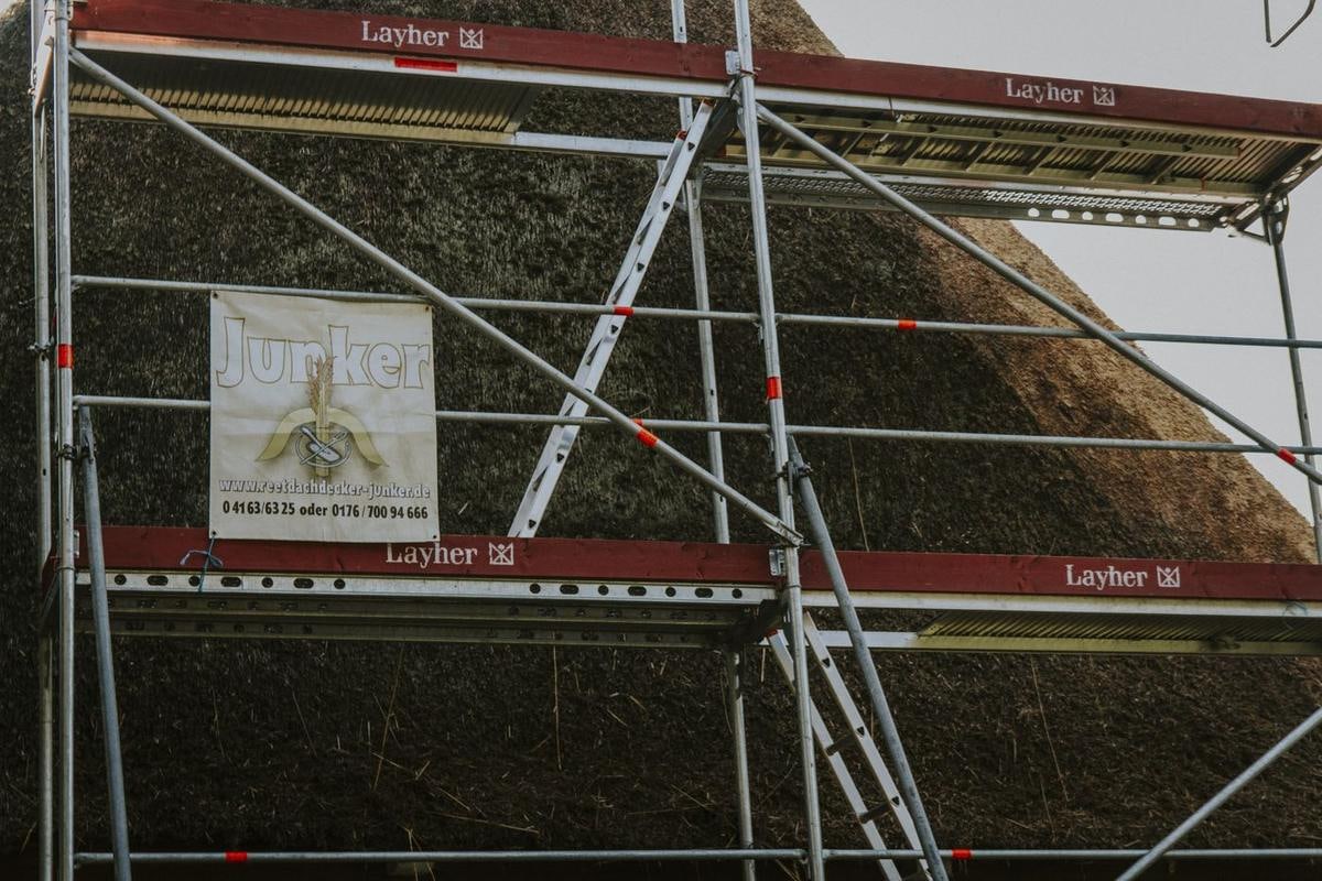 Hohes Gerüst vor einem Reetgiebel mit Schild.