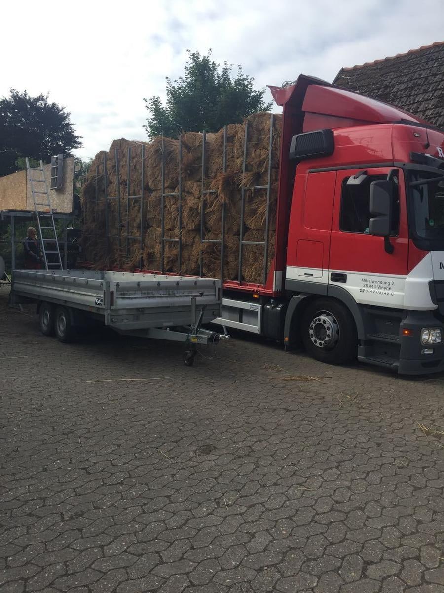 Lastwagen mit Reetbunden auf einem Hof.