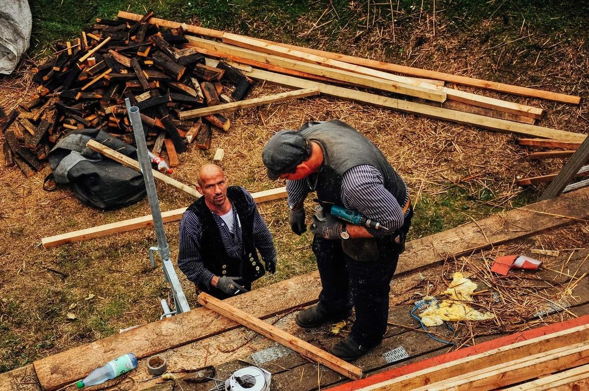 Zwei Männer arbeiten auf einer Dachlattung zwischen Holzresten.