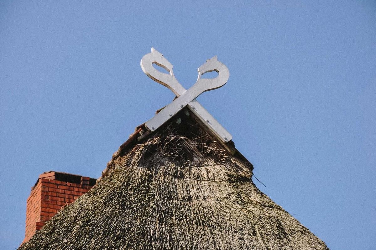 Weiße gekreuzte Bretter auf einem Reetfirst vor blauem Himmel.