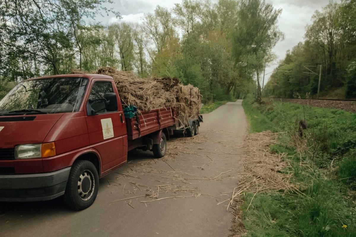Roter Transporter mit voll beladenem Anhänger auf einem Feldweg.