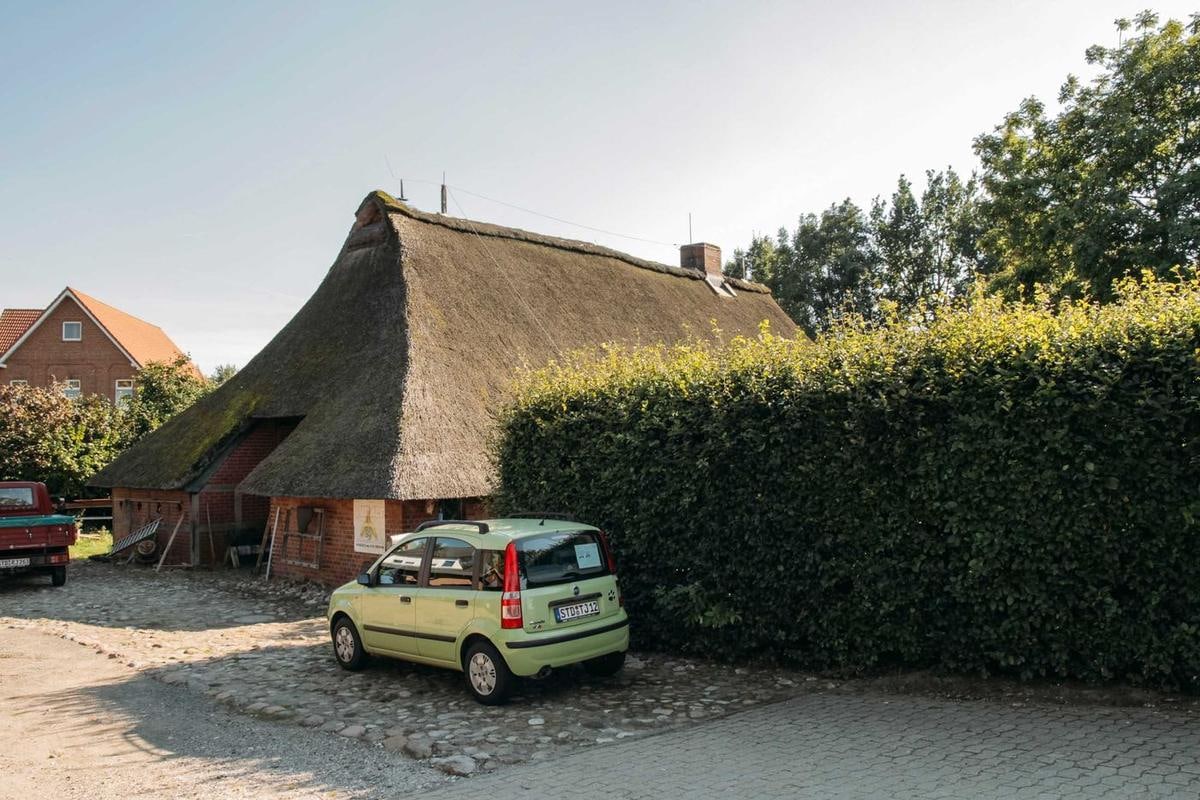 Reetdachhaus mit Hecke, davor ein kleines Auto.