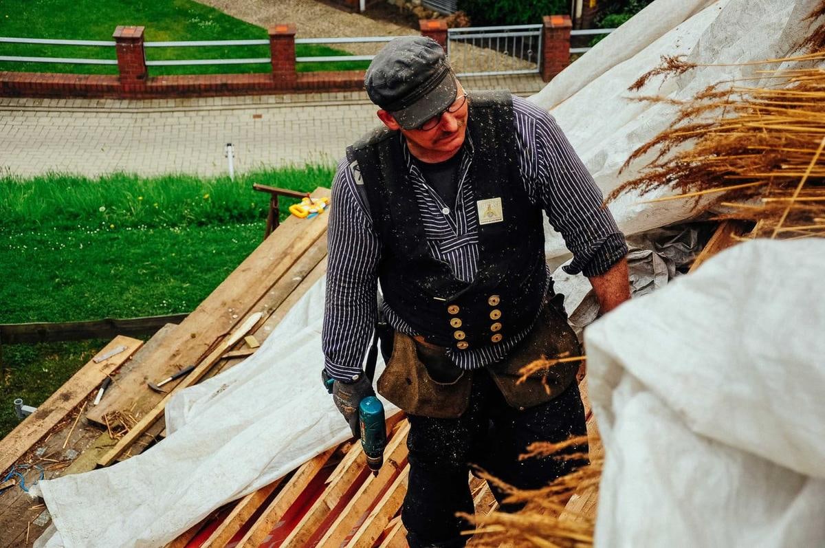 Handwerker in Zunftkleidung kniet zwischen Planen und Holzlatten.