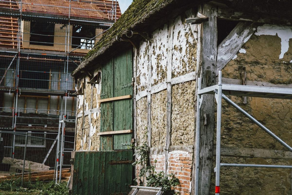 Fachwerkwand mit hellen Lehmfeldern und einem großen grünen Holztor, davor Gerüst.