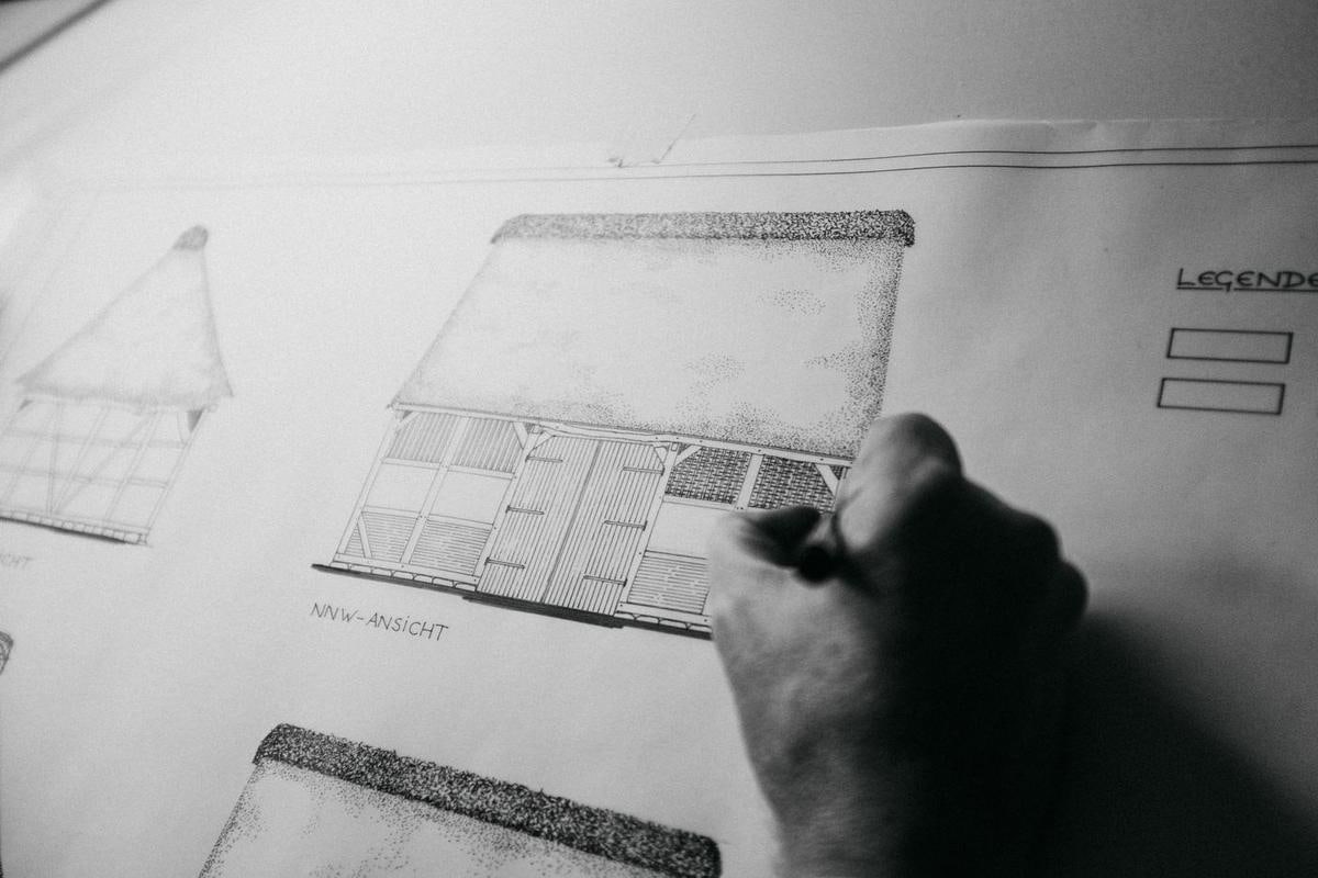 Schwarzweiß: Hand mit Stift über einem Bauplan.