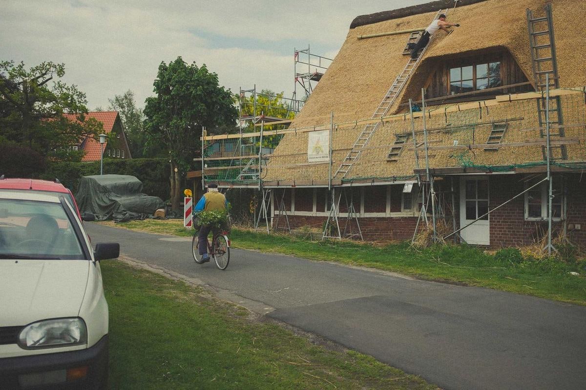 Haus mit Gerüst und neuem Reet an einer Straße, ein Radfahrer fährt vorbei.